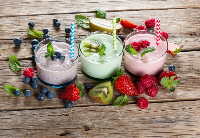 Three fruit smoothies with berries and kiwi on wood