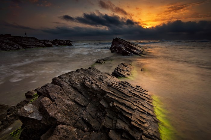 Sunset over rocky coast with person silhouette