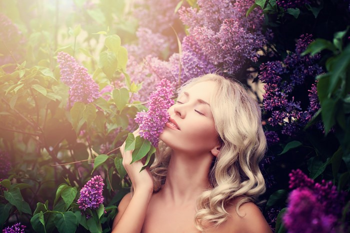 Blonde girl smelling lilac flowers