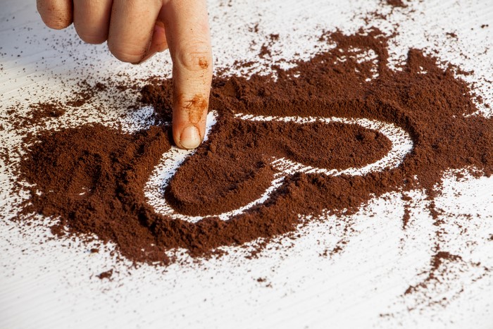 Finger drawing heart in coffee grounds