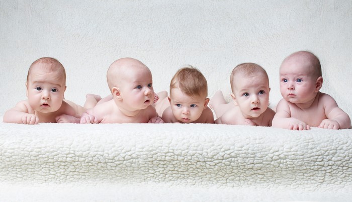 Five infants lying on a white blanket