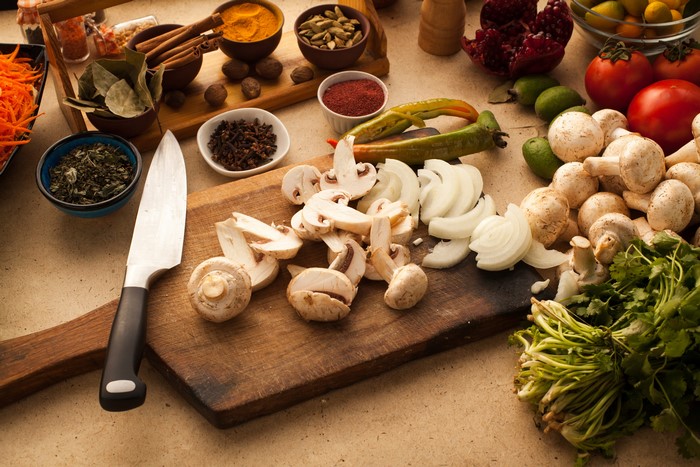 Mushrooms, onions, spices, and knife on cutting board