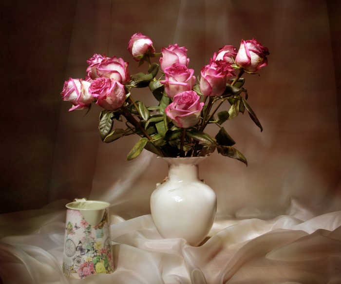Pink and white roses in a vase with a decorative cup