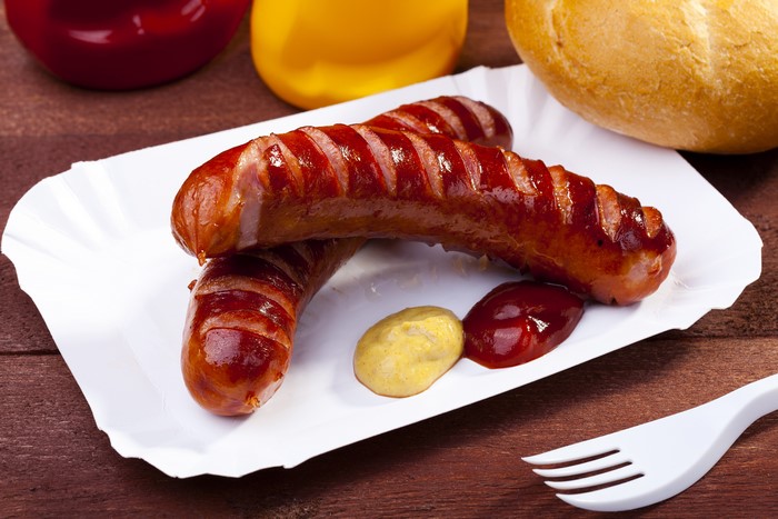 Grilled sausages with mustard and ketchup on a paper plate