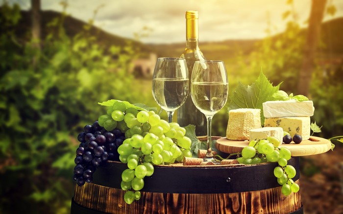 Wine bottle and glasses with grapes and cheese on a barrel