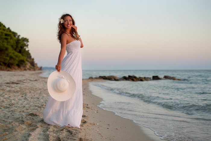 Woman in white dress holding a hat on the beach