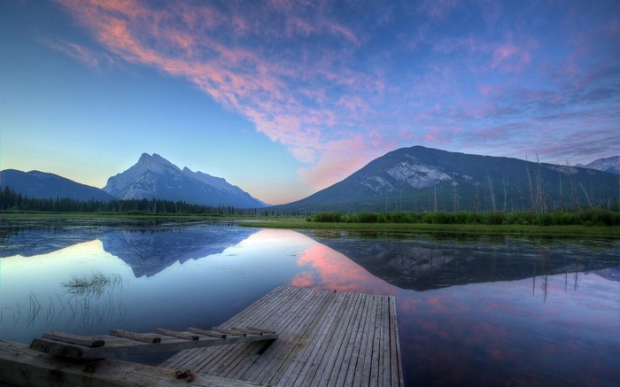 Wooden dock on a calm lake with mountains and pink clouds