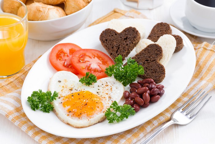 Heart-shaped fried egg breakfast with tomatoes and bread