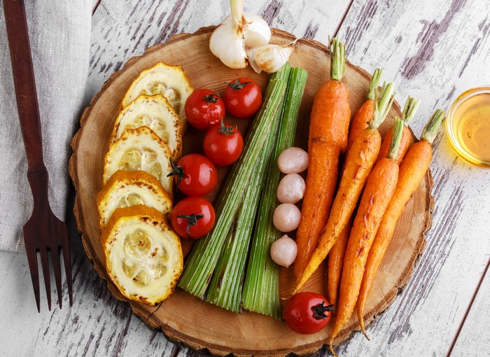 Vegetables including carrots, tomatoes, and garlic on a wooden board