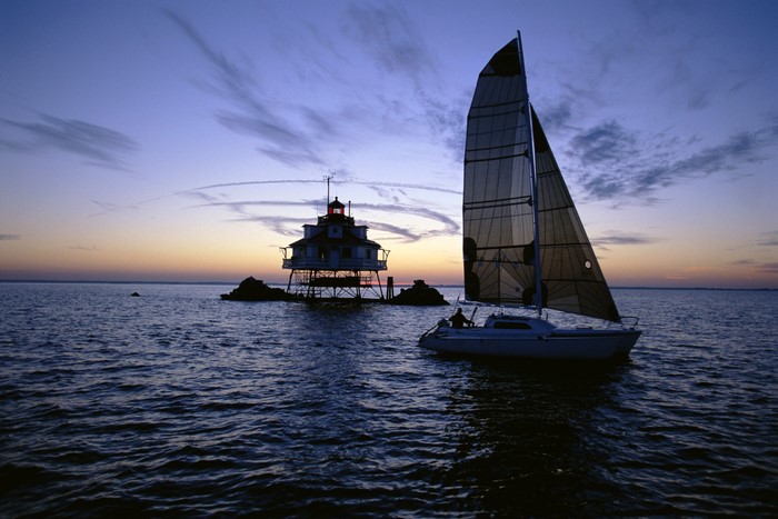 Sailboat and lighthouse at sunset over the sea
