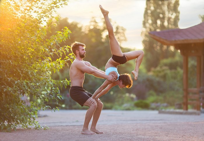 Couple performing acroyoga in a park at sunset