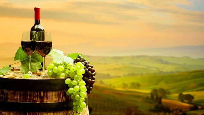 Wine bottle and glasses on barrel with grapes