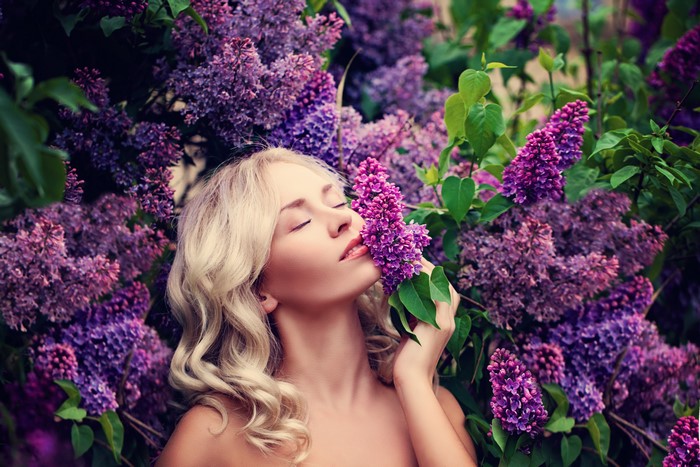 Blonde girl smelling lilac flowers