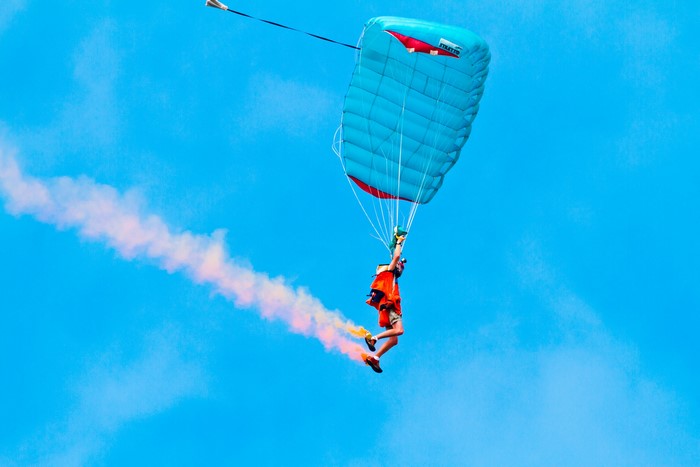 Parachutist with smoke trail against blue sky