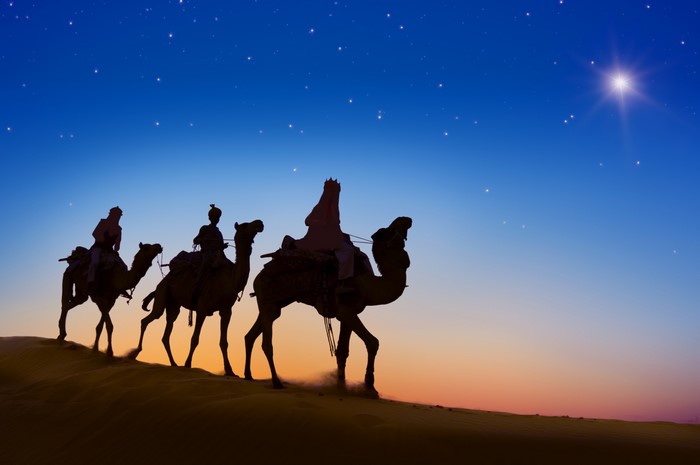 Three Wise Men riding camels under a starry sky