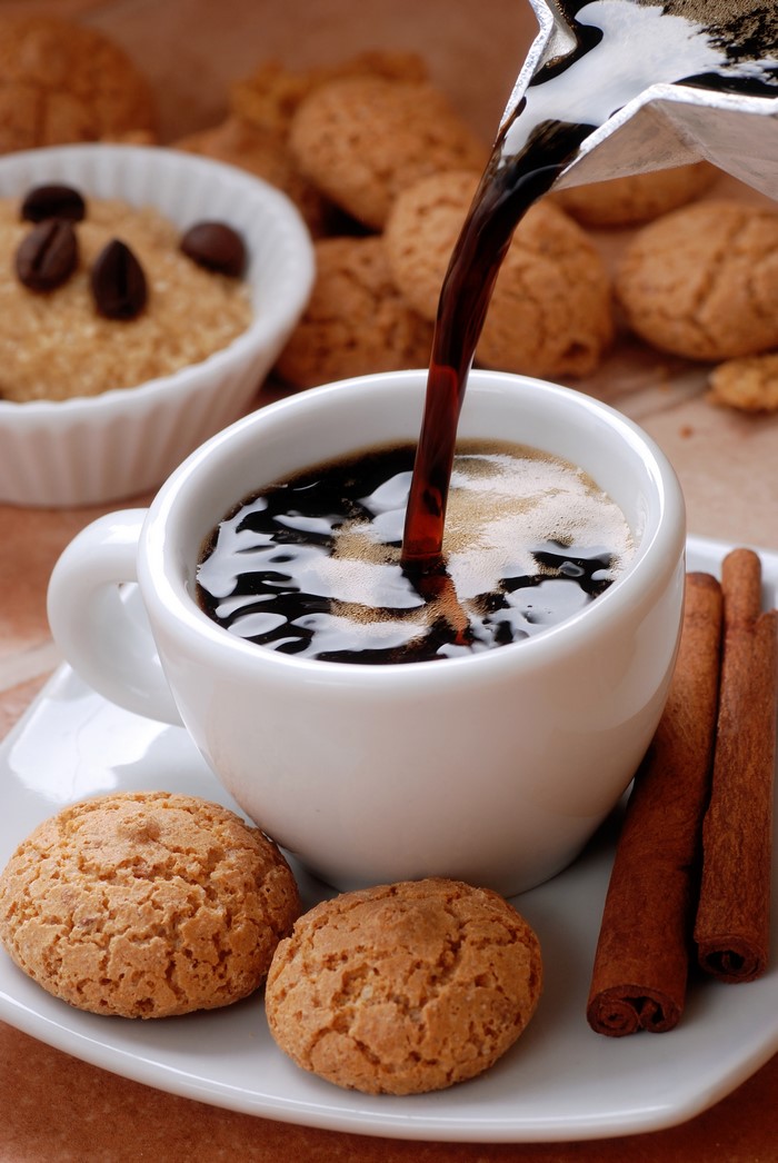 Coffee being poured into a cup with cookies and cinnamon sticks