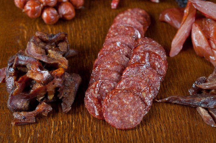 Meat products, sausage, and sliced food on a wooden surface