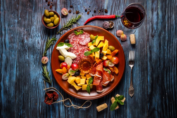 Charcuterie board with salami, ham, cheese, olives, grapes, and wine