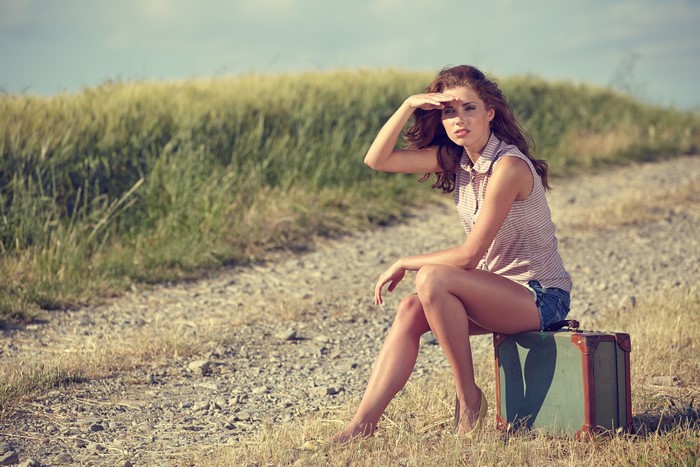Woman sitting on a suitcase by the road