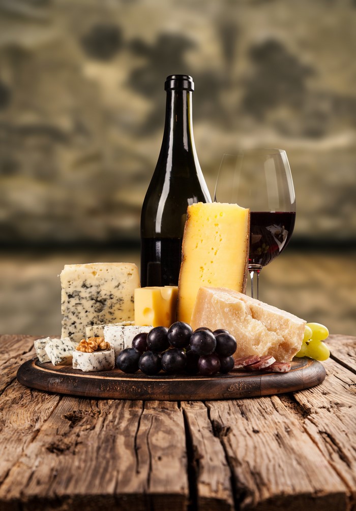 Wine bottle, cheese, grapes, and wine glass on cutting board