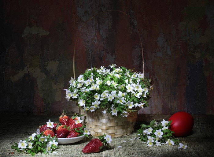 Strawberries and anemones in a wicker basket with a red egg