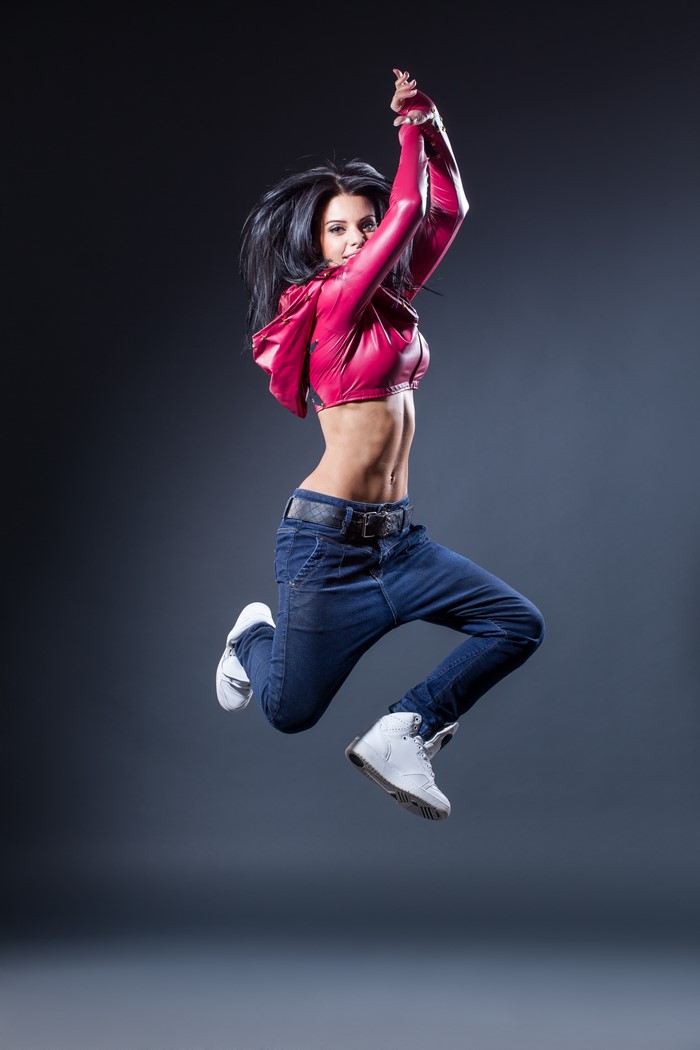 Brunette woman in pink jacket and jeans jumping