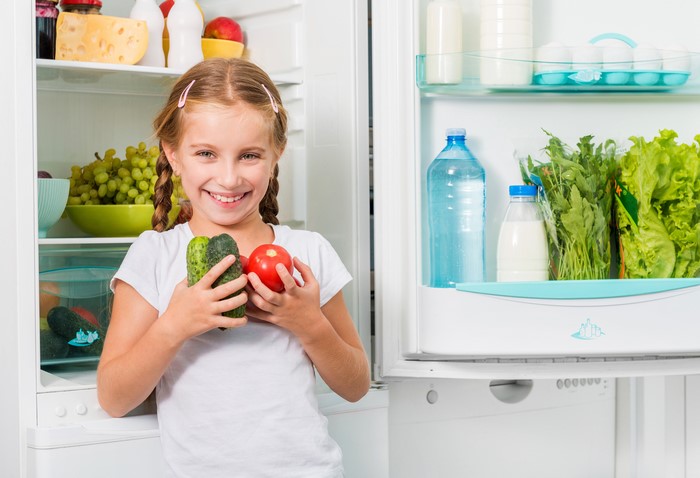 Girl holding vegetables in front of a refrigerator