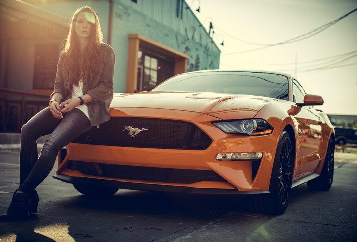 Woman sitting on an orange Ford Mustang