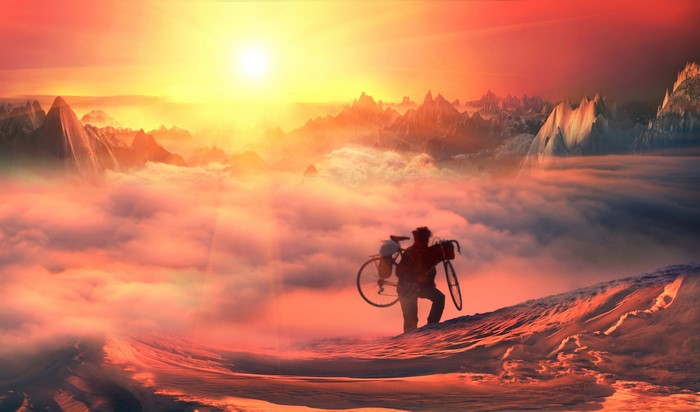 Man carrying bicycle on mountain peak at sunset