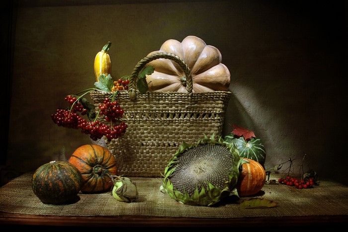 Still life with pumpkins, sunflower, and berries in a basket
