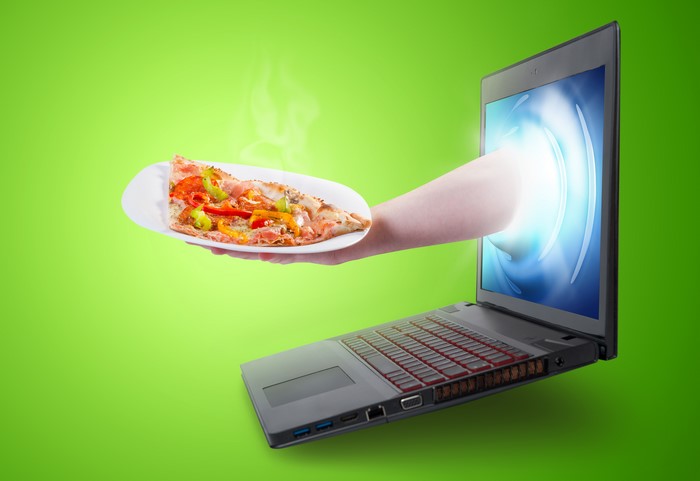 Hand holding pizza slice coming out of laptop