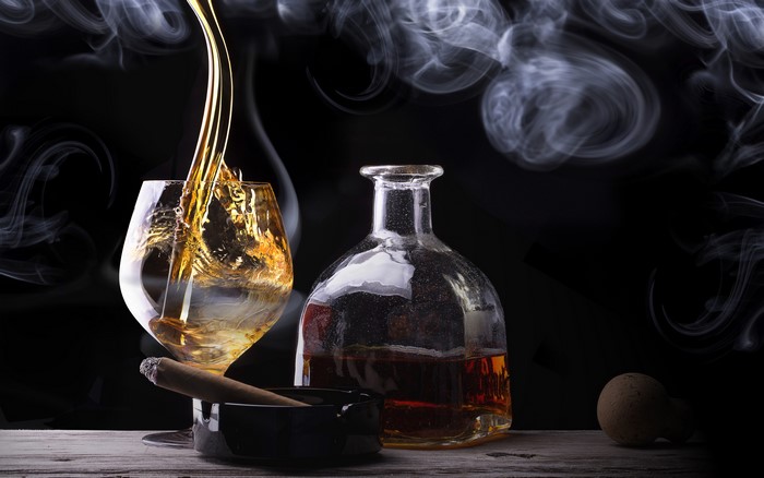 Whisky being poured into a glass with a cigar and bottle
