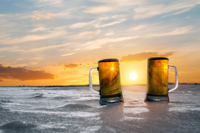 Two beer mugs on ice at sunset