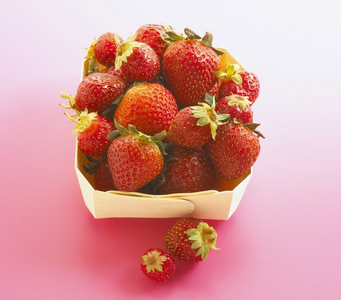 Basket of fresh strawberries on a pink background
