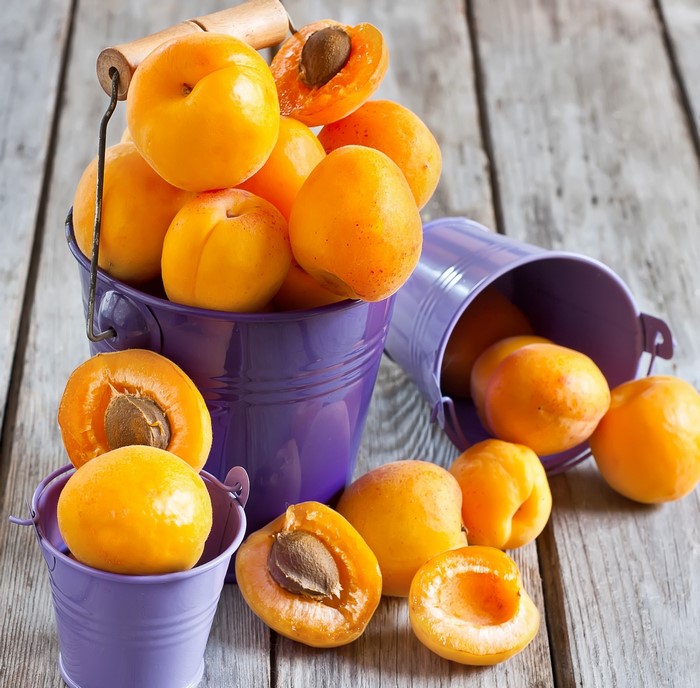 Apricots in purple buckets on wooden planks