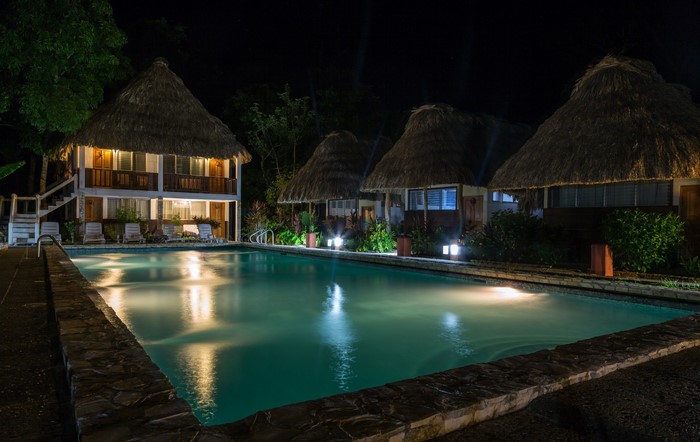 Resort with thatched-roof bungalows and swimming pool at night