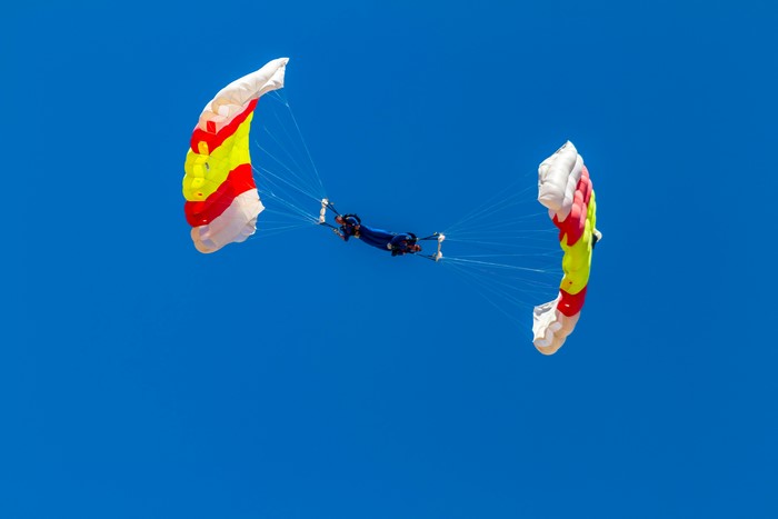 Two skydivers with colorful parachutes against a blue sky