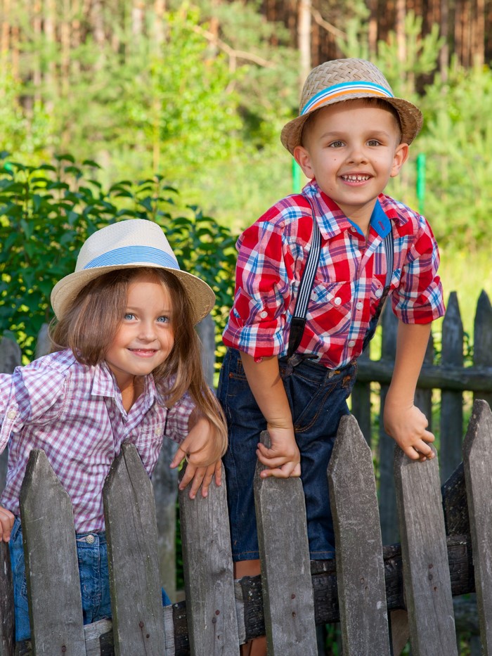 Two children in hats and plaid shirts by a fence