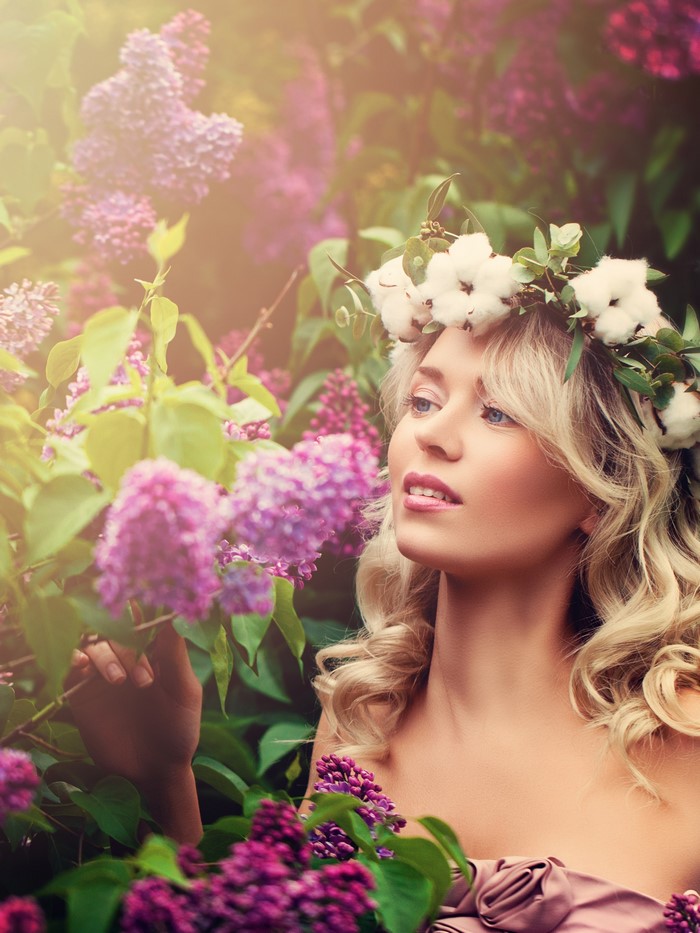 Blonde woman with a flower crown in lilac bushes
