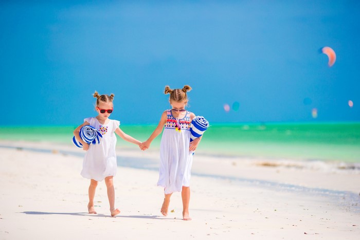 Two little girls in dresses walking on a beach