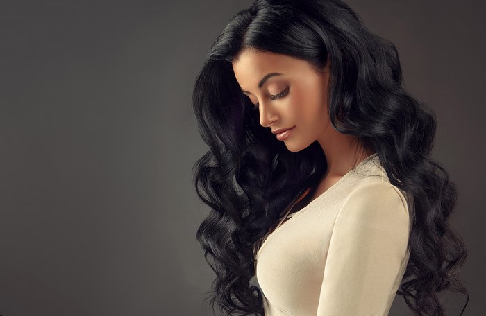Brunette girl with wavy hair on gray background