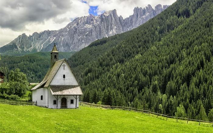 San Sebastiano Chapel in Nova Levante, Italy, with Mountains and Forest