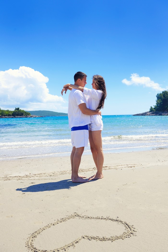 Couple hugging on a beach with a heart drawn in the sand