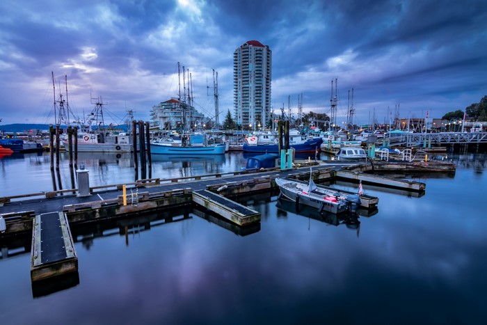 Boats docked in a marina at dusk with a tall building in the background