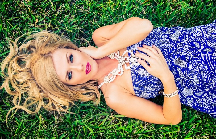 Blonde woman lying on grass wearing blue dress and jewelry