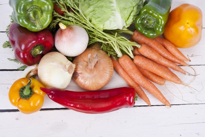 Vegetables including bell peppers, carrots, and onions on wood planks