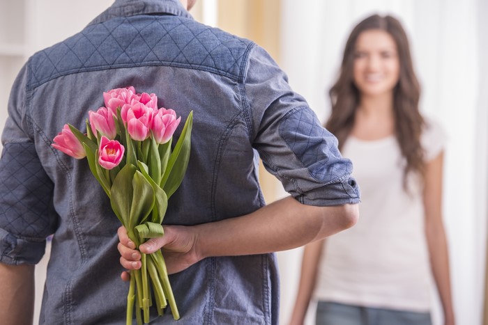Man hiding pink tulips behind his back from woman