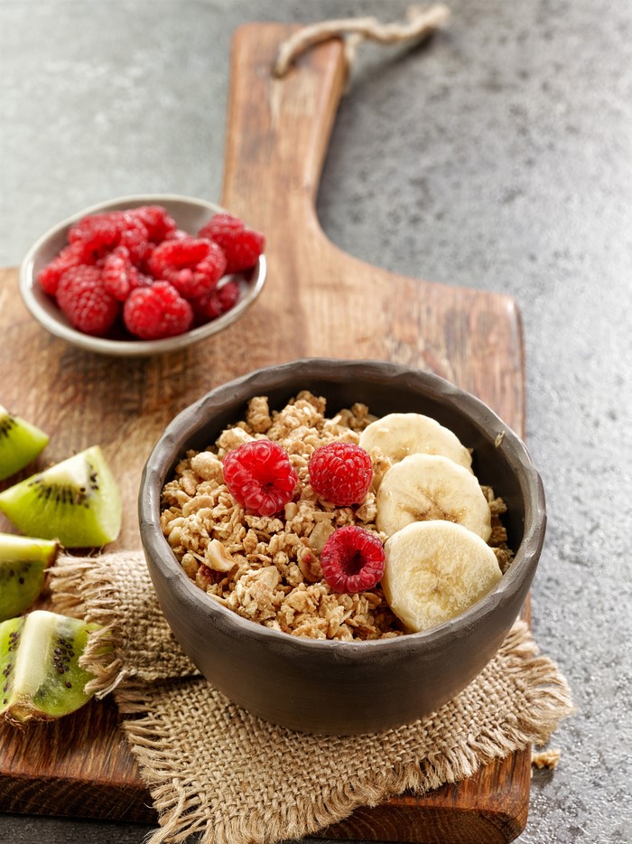 Muesli with raspberries, bananas, and kiwi on a cutting board