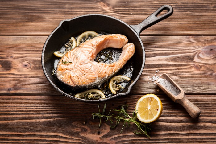 Salmon steak with lemon slices in a cast iron pan