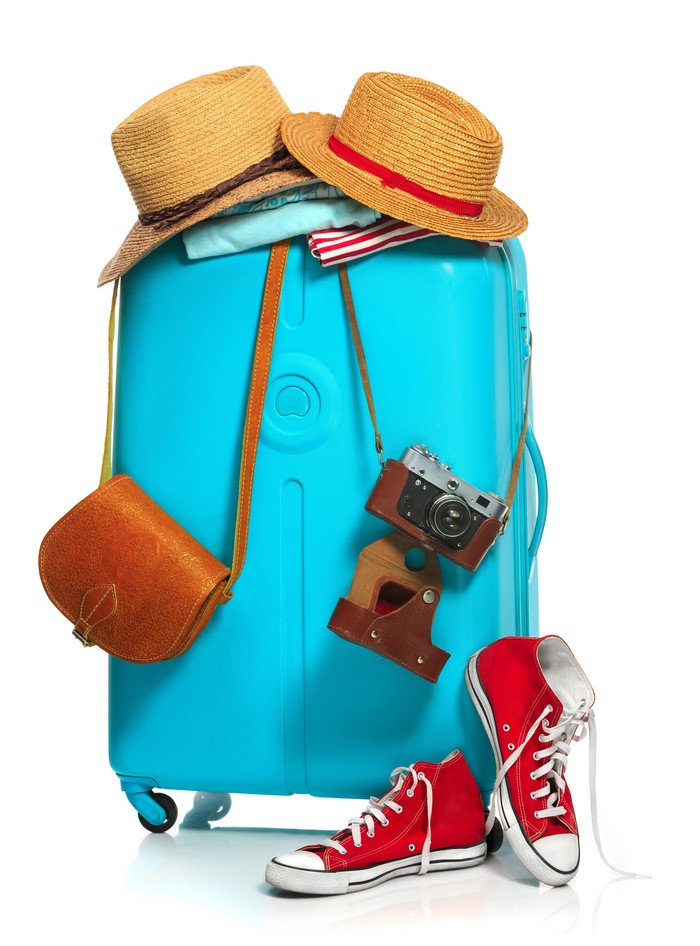 Turquoise suitcase packed with travel items including hats, camera, and shoes